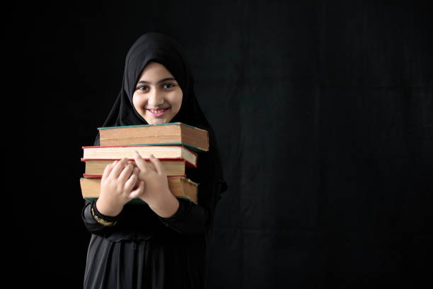 chica musulmana sosteniendo un montón de libros sobre fondo negro - nikab veil islam arabia fotografías e imágenes de stock