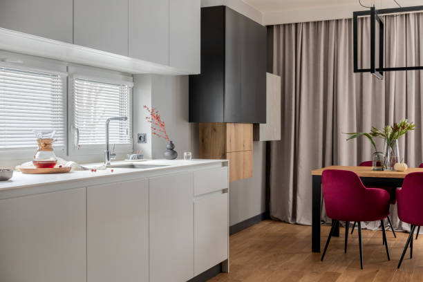 istock Stylish composition of kitchen and dining room open space interior. Minimalist ergonomic kitchen space. Velvet chairs, wooden table and personal accessories in the modern dining room. Template. 1384256048