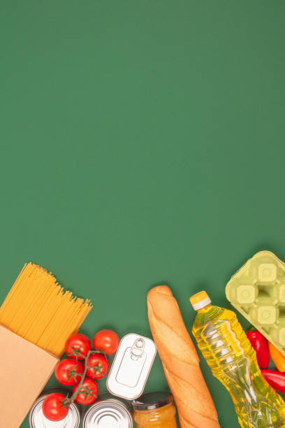 istock Vertical image with groceries, food donations on green background with copy space - pasta, vegatables, canned food, baguette, cooking oil, tomatoes. Food bank, food delivery, support refugees concept 1384256831