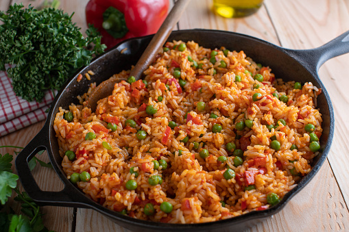 Homemade fresh cooked serbian rice with bell peppers, green peas and aivar. Served with wooden spoon in a rustic cast iron pan on wooden table. Closeup and ready to eat