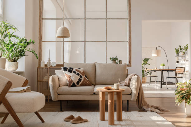 istock Elegant living room interior design with beige modern sofa, side table and creative accessories. Template. Copy space. Dining room in the background. 1384258145