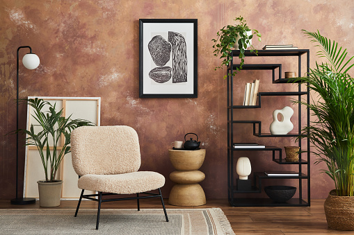 Stylish living room interior design with mock up poster frame frotte armchair, black metal shelf, side table, plants and creative home accessories. Home staging. Template. Copy space.
