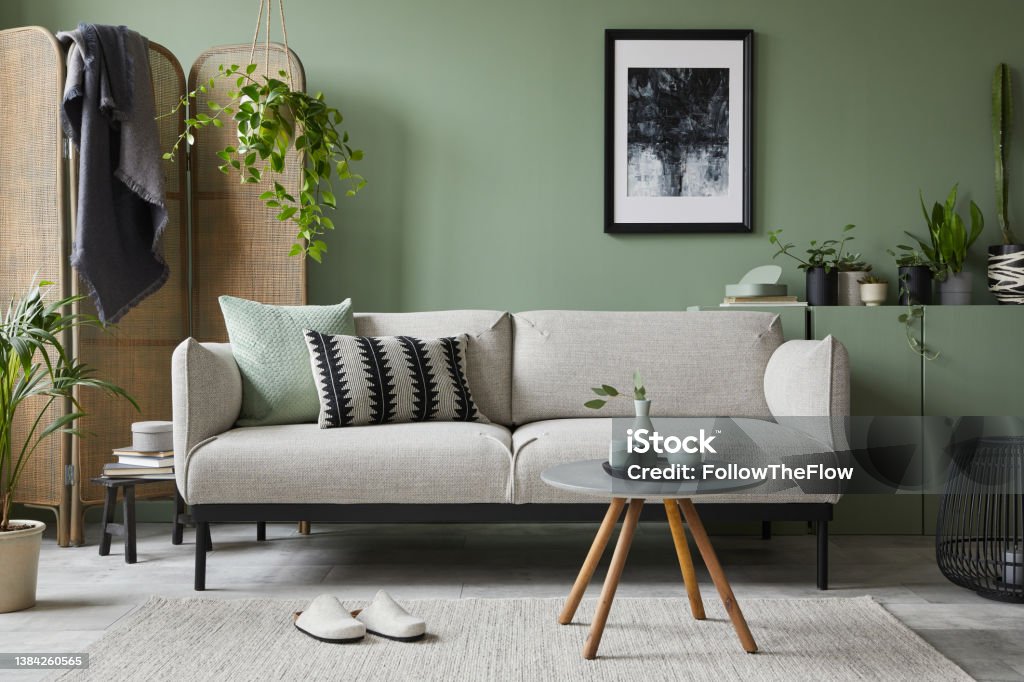 Stylish composition of modern living room interior. Mock up poster frame, modern sofa, folding screen, plants and personal accessories. Sage green wall. Home staging. Template. Copy space. Home Interior Stock Photo