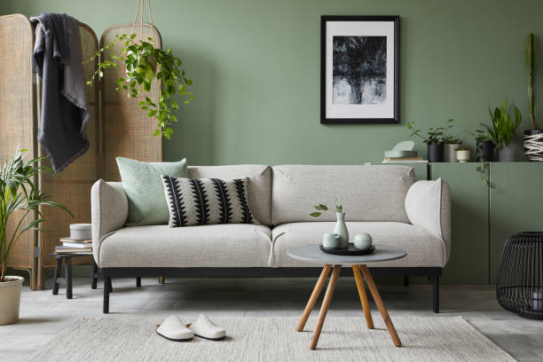 Stylish composition of modern living room interior. Mock up poster frame, modern sofa, folding screen, plants and personal accessories. Sage green wall. Home staging. Template. Copy space. stock photo