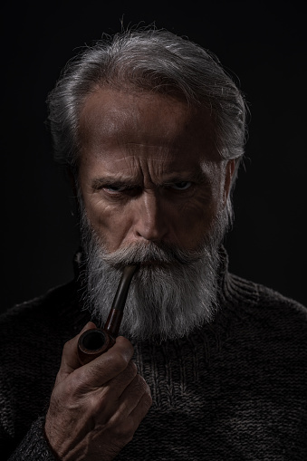 Portrait of bearded redhead English male. Senior smoking pipe in a studio.