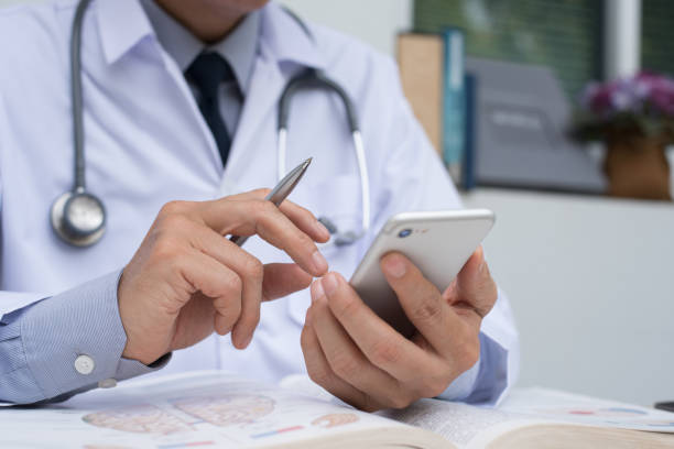 doctor using smartphone and reading book - medical student healthcare and medicine book education imagens e fotografias de stock