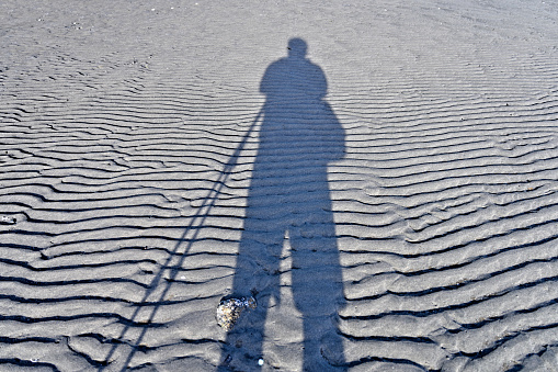 A beautiful view looking at at the shadow of a morning walker along the sandy beach equipped with trekking poles