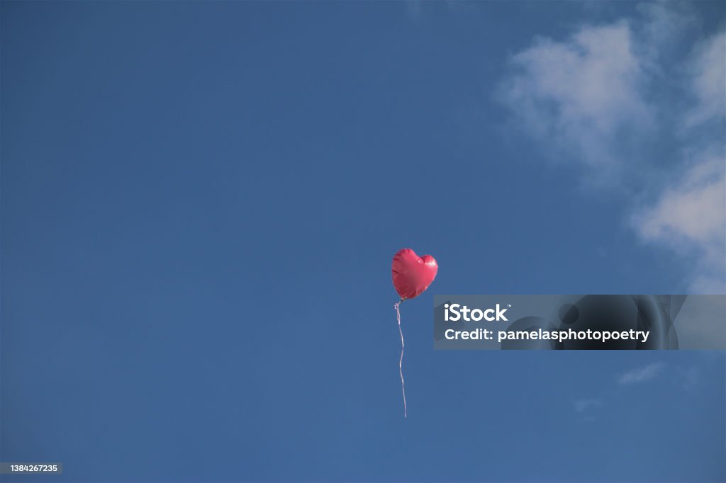 Love is in the Air Single object pink heart shaped balloon floating midair in light breeze against beautiful blue sky wispy white clouds minimalist negative space for copy. Joy Stock Photo