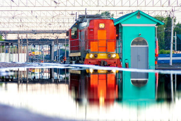 Kemerovo, Russia, 23 June 2021 - red diesel locomotive at station is reflected in huge puddle on platform formed from mistakes made in designing the surface of the passenger platform, selective focus