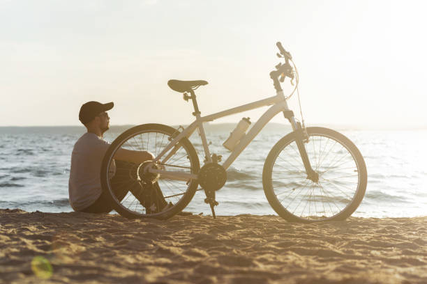 istock male cyclist is resting sitting on a sandy beach 1384269546