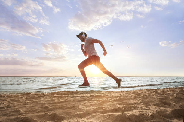 istock sporty man running on a sandy beach at sunset 1384269666