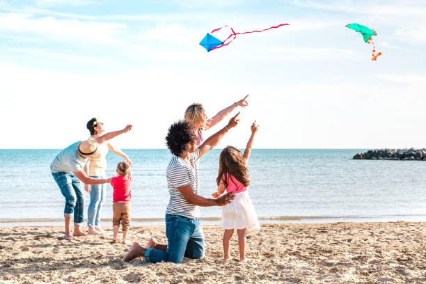 해변 휴가에서 연을 가지고 노는 부모와 아이들이 작곡 한 여러 가족 - 해변에서 함께 즐거운 솔직한 사람들과 여름 기쁨 생활 스타일 개념 - 밝은 생생한 필터 - beach women joy sand 뉴스 사진 이미지