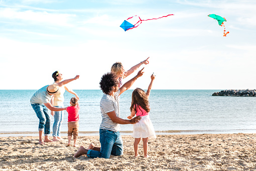 Multiple families composed by parents and children playing with kite at beach vacation - Summer joy life style concept with candid people having fun together at seaside - Bright vivid filter