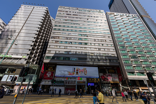 Hong Kong - March 10, 2022 : Pedestrians walk past the Chungking Mansions in Nathan Road, Tsim Sha Tsui, Kowloon, Hong Kong. This building features many shops, guesthouses, curry restaurants, and foreign exchange offices.