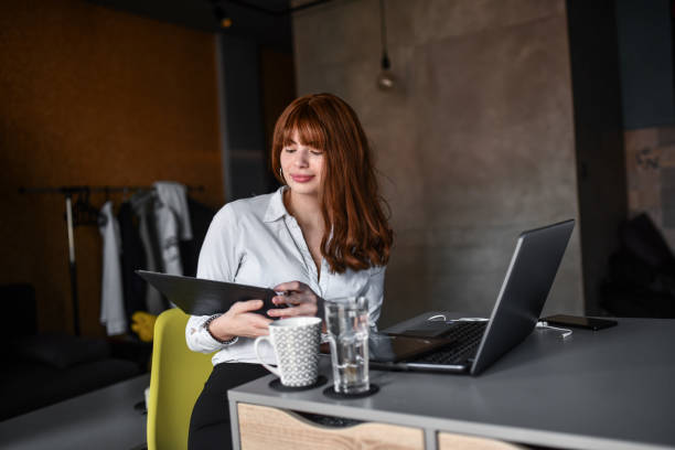 istock Redhead Female Analyzing Statistics From Work At Home With Clipboard And Laptop 1384276112
