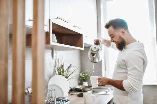 Photo of Focused Bearded Male Pouring Hot Water In Cups In Kitchen