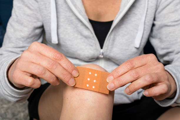 woman sticks a plaster on her injured knee stock photo