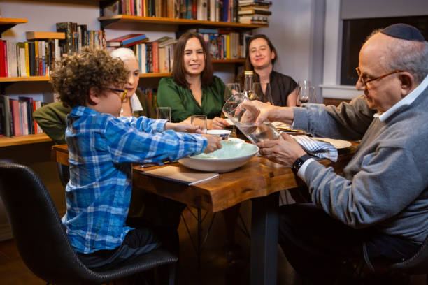 un grand-père aide un petit garçon à se laver les mains au seder de la pâque avec sa famille - seder passover judaism family photos et images de collection