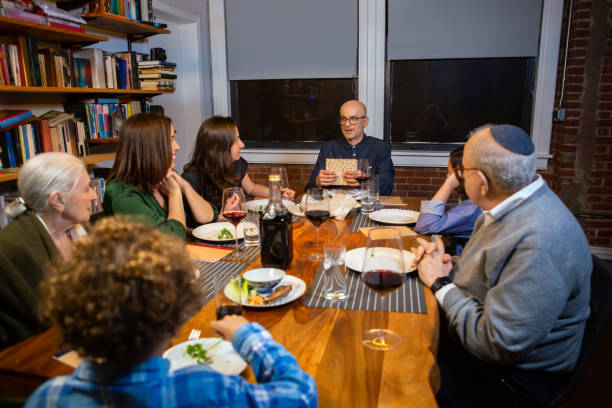 Seder Leader Holding Up Matzo A modern Jewish American family celebrates Passover together. The Seder leader holds up the middle matzo before breaking it. passover celebration stock pictures, royalty-free photos & images