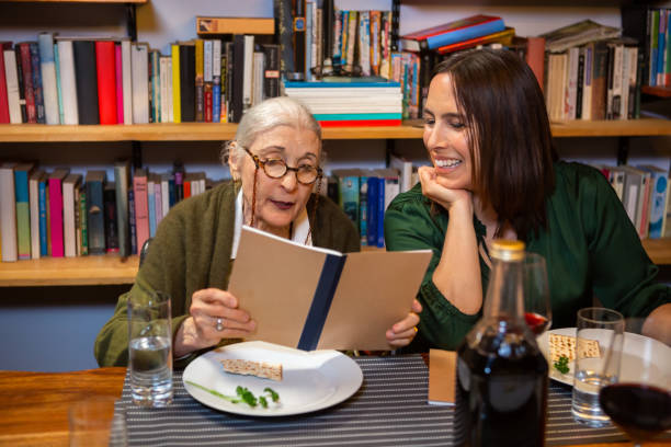 Two Women Reading from Haggadah at Passover Seder A modern Jewish American family celebrates Passover together. passover celebration stock pictures, royalty-free photos & images