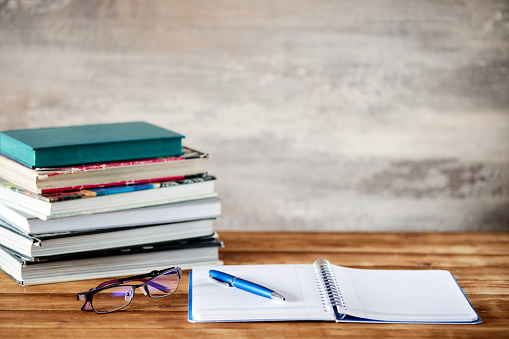 Pile of books, a notebook, pen and a pair of eyeglasses on the desk. Education concept.