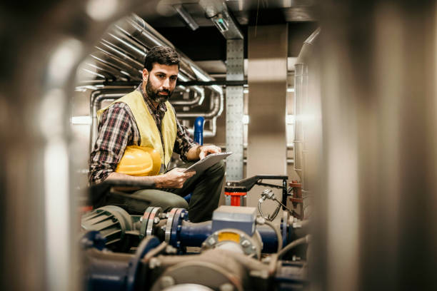 Technician engineer man in uniform with tablet checking and control boiler tanks and liquid pipeline in production line at factory Technician engineer man in uniform with tablet checking and control boiler tanks and liquid pipeline in production line at factory heating engineer stock pictures, royalty-free photos & images