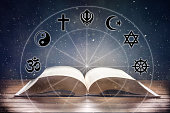 istock Book on wooden table with religious symbology and universe background 1384293036