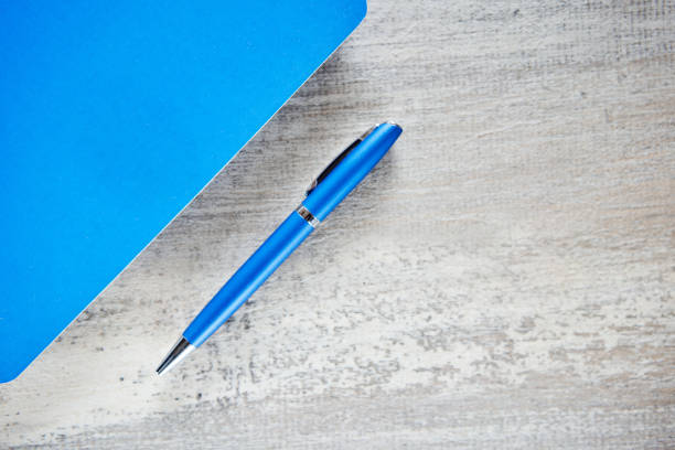 Blue notebook and blue pen on wooden desk. View from above