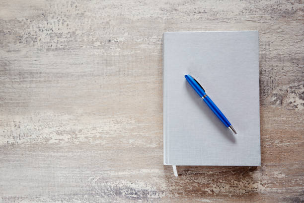 istock Grey notebook and blue pen on wooden desk. 1384297615