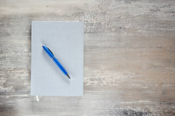 istock Grey notebook and blue pen on wooden desk. 1384297622