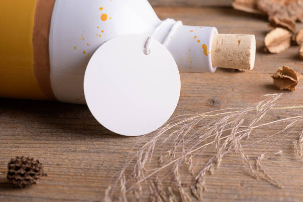 istock Round white tag mockup on ceramic bottle for olive oil a wooden background with boho decoration, element for packing 1384299803