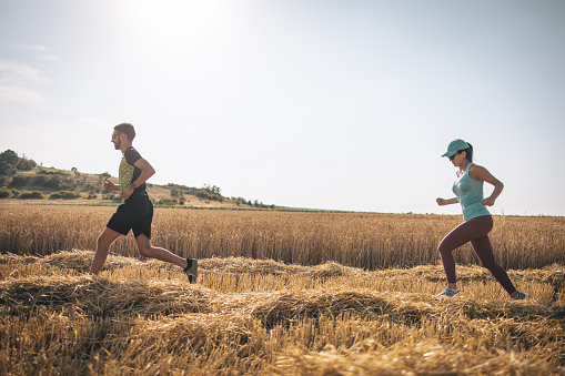 Man and woman jogging together on wheat field on a lovely summer day.
