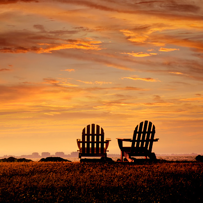 Rear view of two empty Adirondack Chairs and sunset