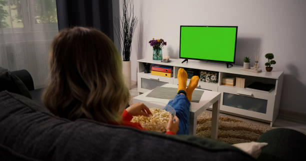 Young Woman Watching Television with Green Screen Chroma Key, shot behind models shoulders. Girl Eating Popcorn Relaxing Sitting on a Couch Home looking to TV. Young Woman Watching Television with Green Screen Chroma Key, shot behind models shoulders. Girl Eating Popcorn Relaxing Sitting on a Couch Home looking to TV. wasting time stock pictures, royalty-free photos & images