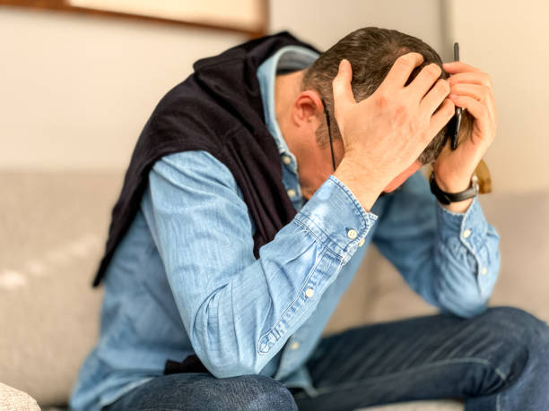 istock Middle aged man sitting on sofa at home in the morning before going to office and checking news. Head in hands 1384330192