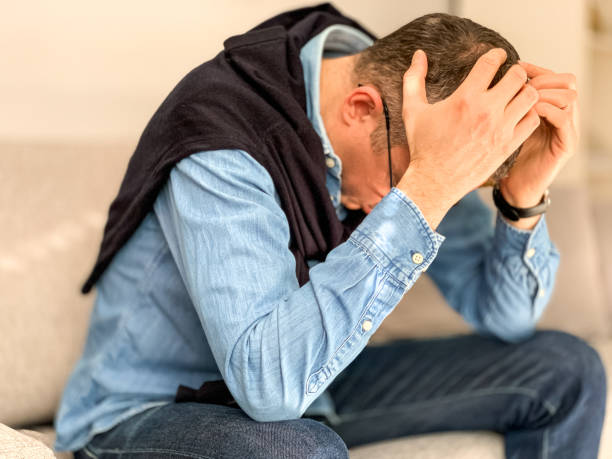 istock Middle aged man sitting on sofa at home in the morning before going to office and checking news. Head in hands 1384330218