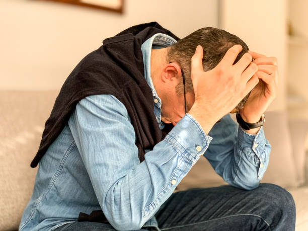 istock Middle aged man sitting on sofa at home in the morning before going to office and checking news. Head in hands 1384330309