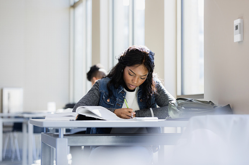 A pretty Asian female college student is holding her books and the United Kingdom flag, standing against a yellow, isolated background. Exchange student and study abroad concept