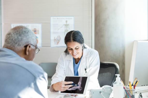 Orthopedic surgeon uses x-ray displayed on tablet to help patient The mid adult female orthopedic surgeon uses the x-ray displayed on the digital tablet to help the unrecognizable senior adult man understand his injury. orthopedist stock pictures, royalty-free photos & images