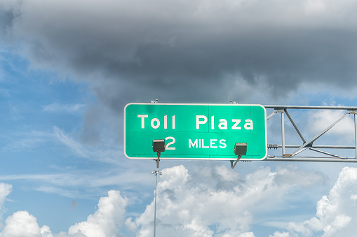 Sign for Toll Plaza in 2 miles lane for i75 interstate highway from Miami to Naples in Florida and clouds in blue sky