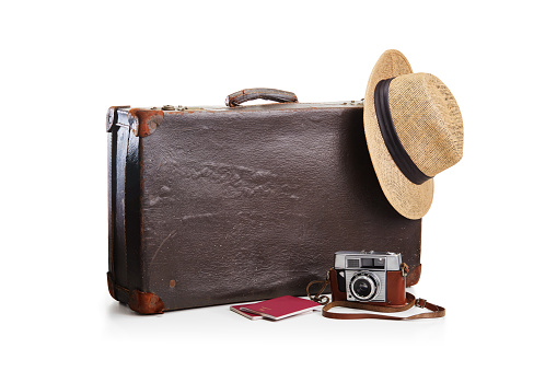 Old fashioned vintage brown leather suitcase with a film camera, a straw hat and two passports on white. Ready for travel and holiday concept