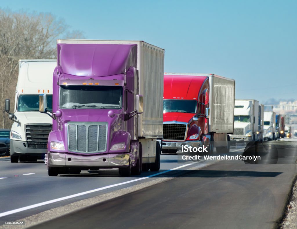 Multi-colored Convoy of Big Trucks Rolls Down The Interstate Horizontal shot of a multi-colored convoy of big trucks rolling down the interstate. Truck Stock Photo