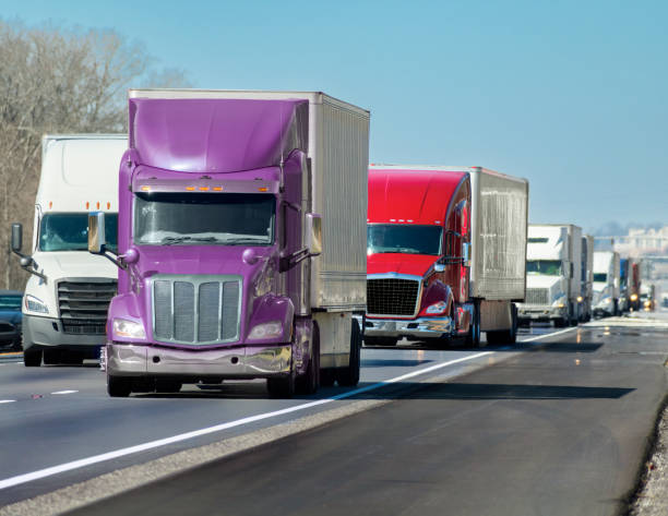 Multi-colored Convoy of Big Trucks Rolls Down The Interstate Horizontal shot of a multi-colored convoy of big trucks rolling down the interstate. convoy stock pictures, royalty-free photos & images