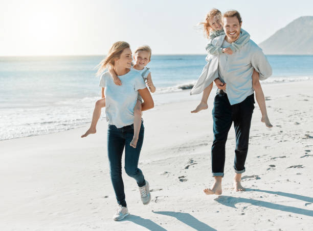 istock Shot of a couple carrying their daughters on their backs while at the beach 1384341665