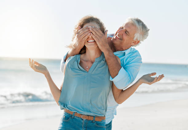 снимок мужчины, закрывающего глаза своей жене во время пребывания на пляже - love anniversary lifestyles outdoors стоковые фото и изображения