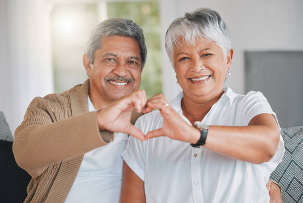 Portrait of a senior couple making a heart shape with their hands at home I wrote your name in my heart and forever it will stay heart hands multicultural women stock pictures, royalty-free photos & images
