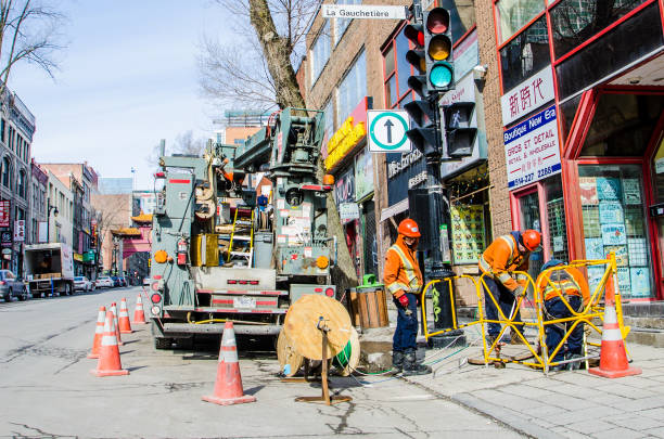 City blue collar workers close to manhole on sidewalk of Chinatown of Montreal during day of winter.They will deploy electrical wires from a spool