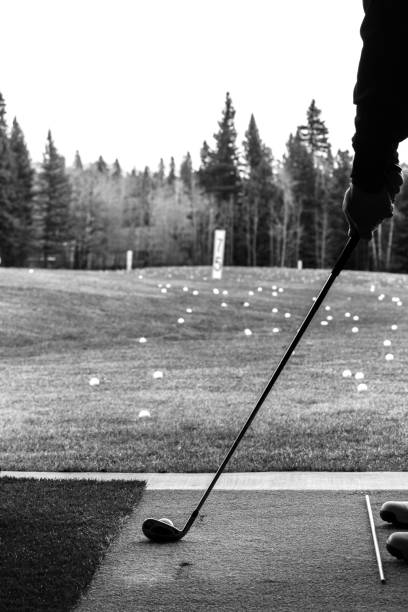 istock Black and white silhouette of man practicing golf at a driving range standing in practice facility with golf range, range balls and forest in the background. 1384350705