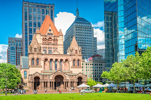 Pedestrians walk in front of Trinity Church on Copley Square in downtown Boston, Massachusetts, USA on a sunny day.