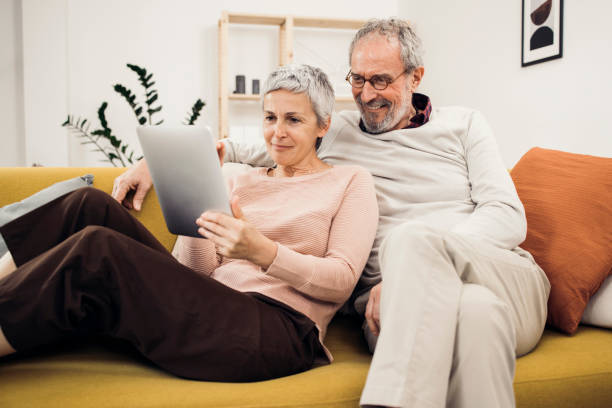 istock Happy senior couple relaxing on the sofa and using tablet 1384369386